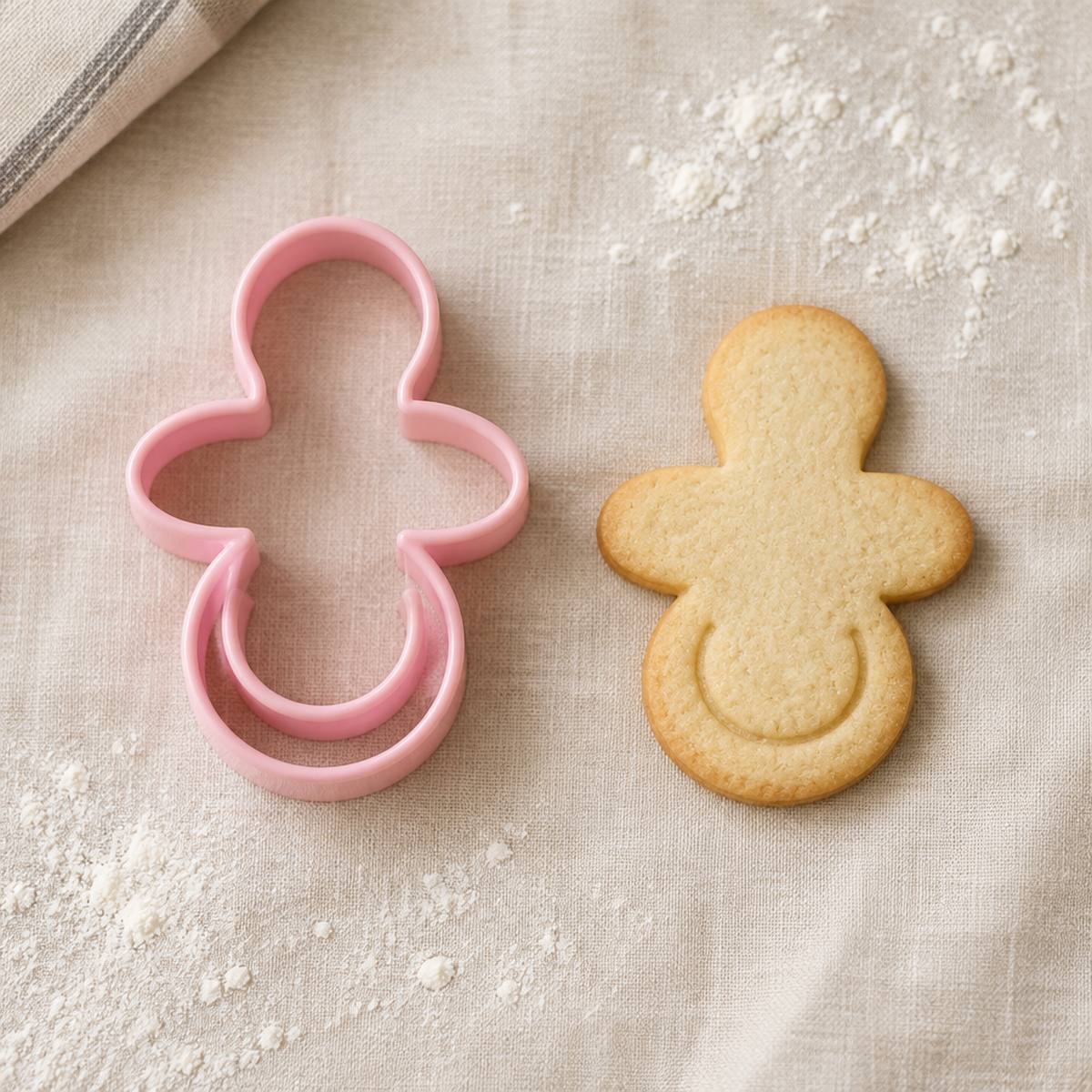 Cortador de galletas con forma de chupete junto a una galleta horneada con la misma forma