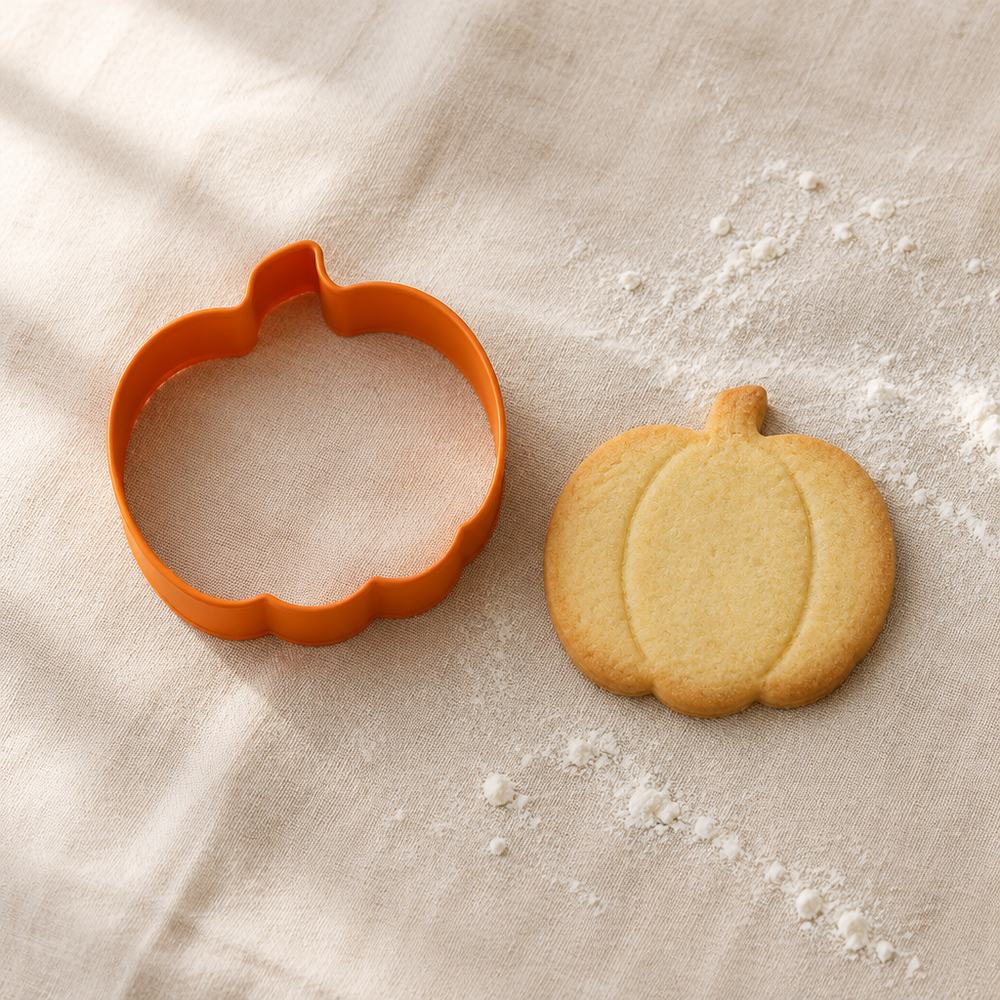 Cortador de galletas con forma de calabaza junto a una galleta horneada con la misma forma