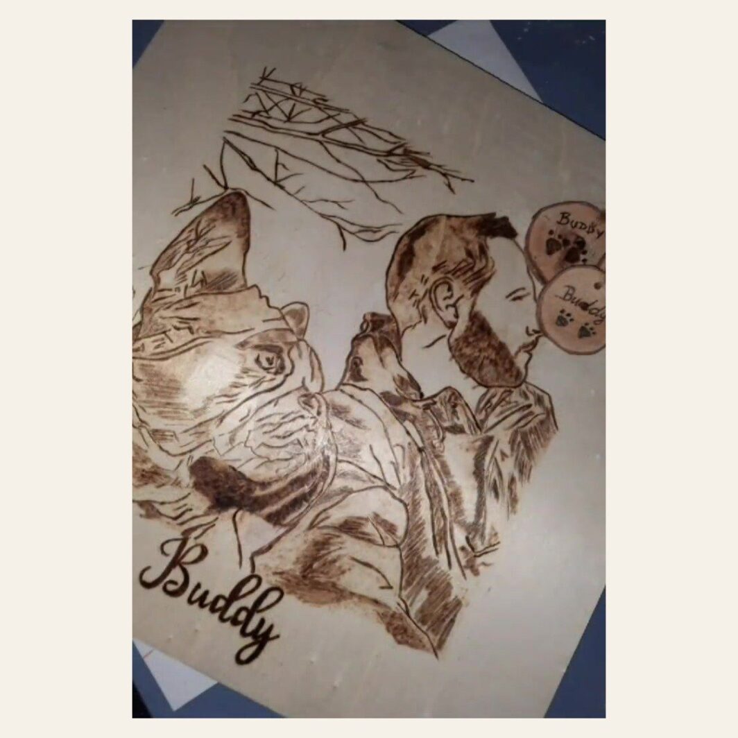 Cuadro de madera pirograbado a mano con el retrato de Buddy, un perro, junto a su dueño, con su nombre grabado debajo